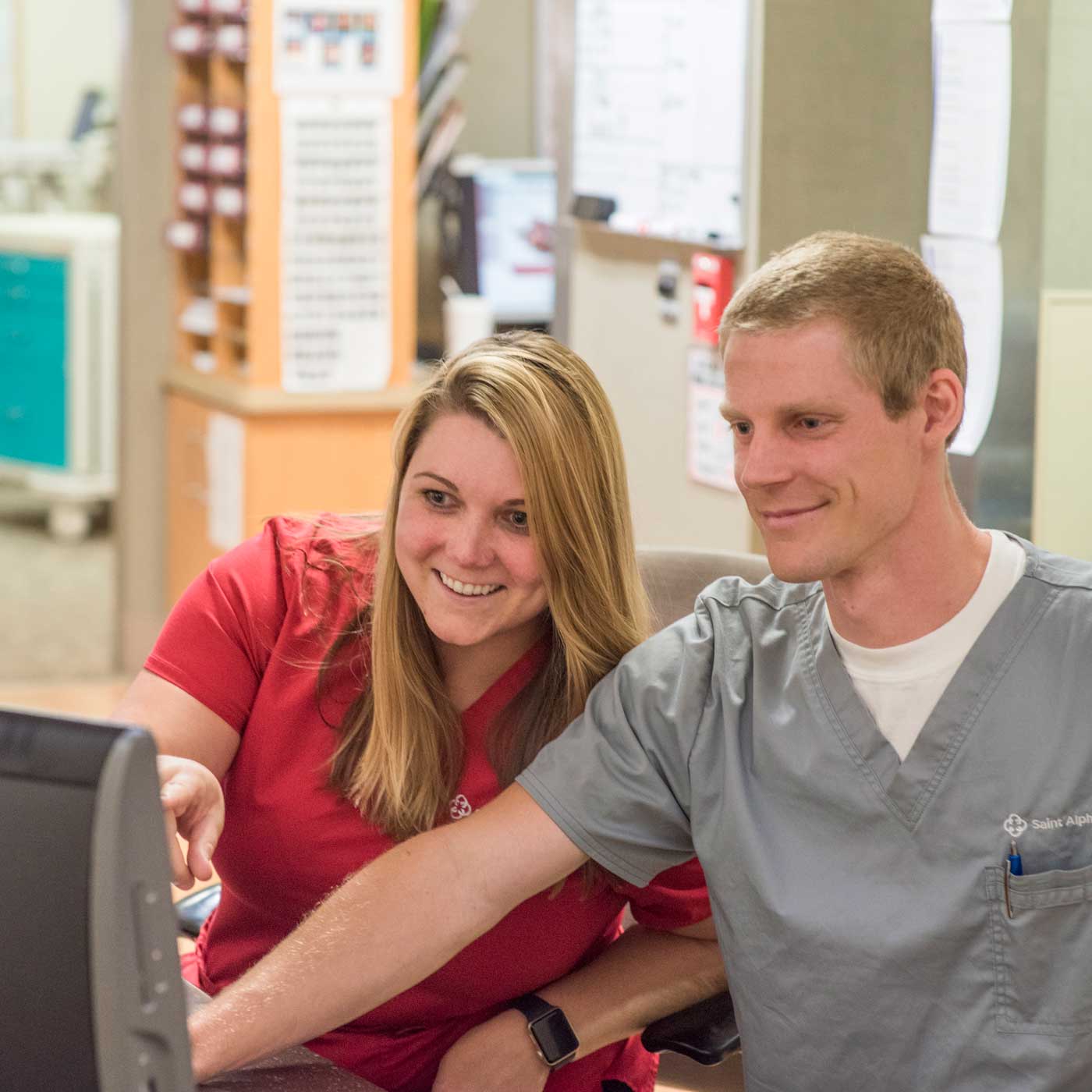 An instructor and student in scrubs in a hospital looking at a computer screen together.